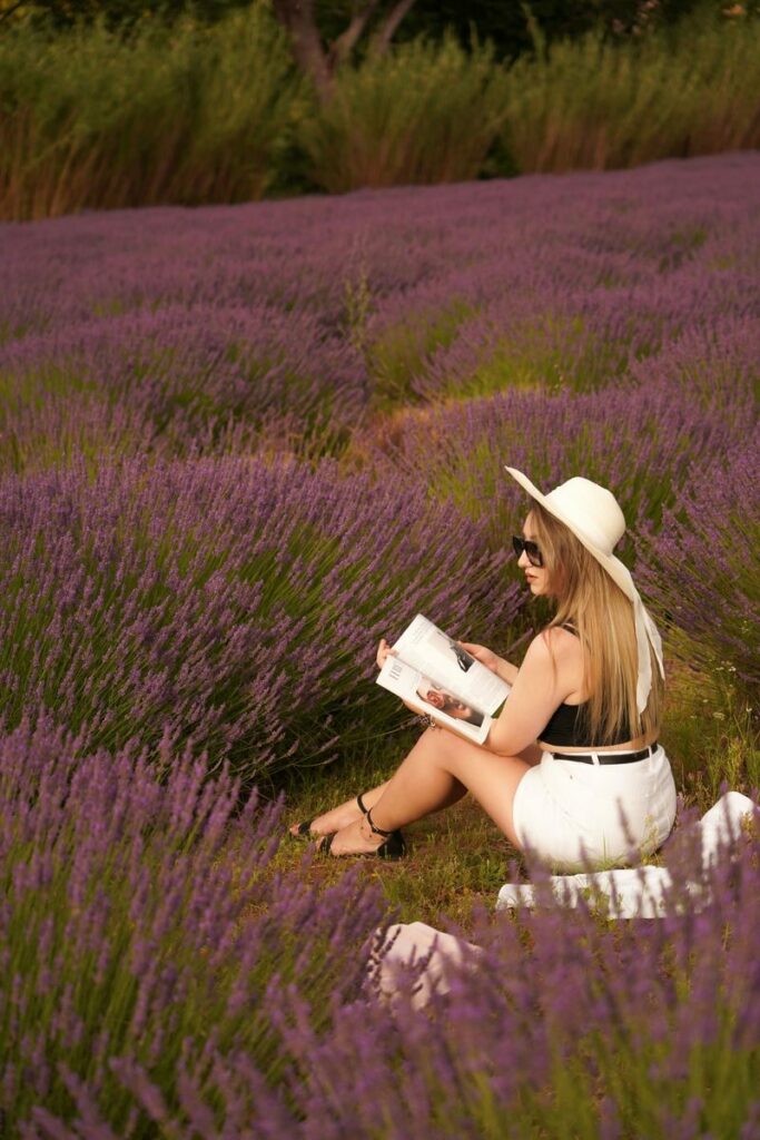 A woman in a hat reads a book amidst blooming lavender fields, capturing summer tranquility.